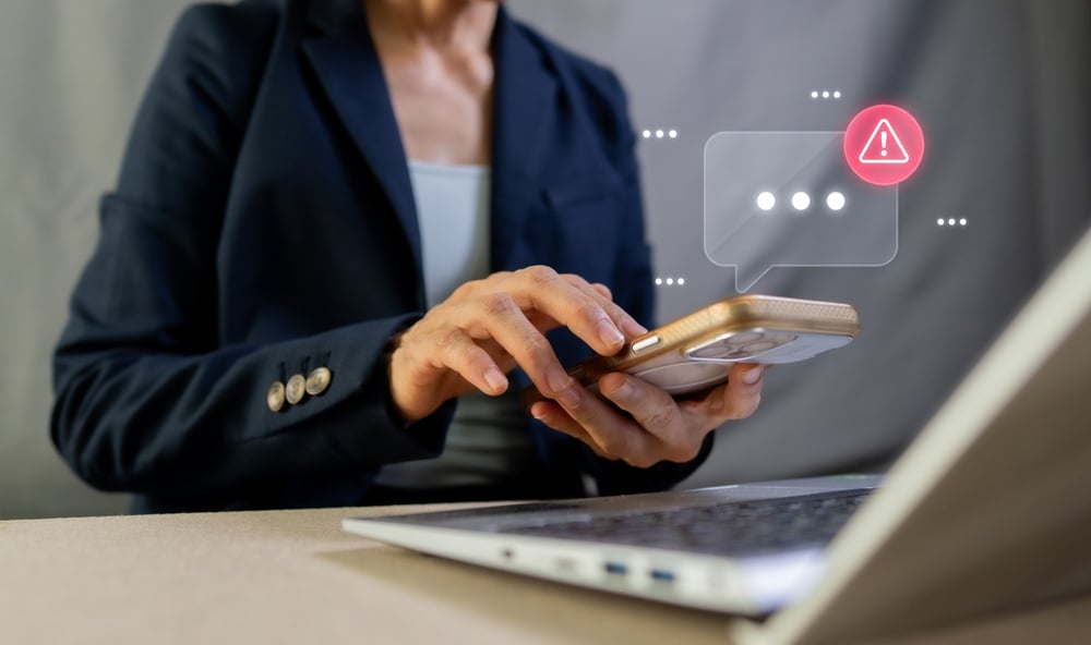 Business woman using her mobile phone which appears to be flagging some security risks